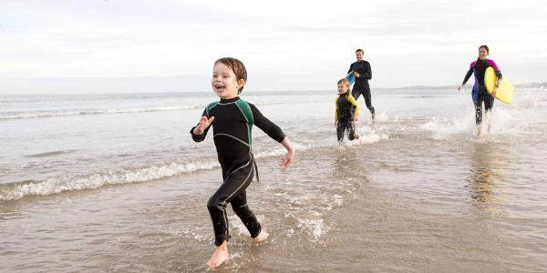 Family in wetsuits running on a beach