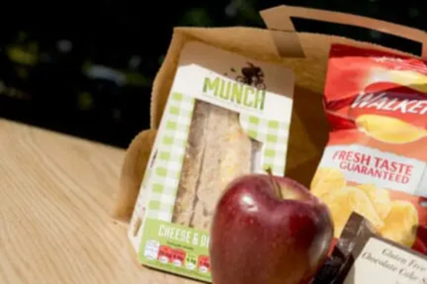 Brown paper bag containing a sandwich, packet of crisps and an apple
