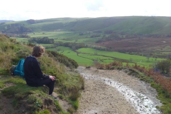 Boy sat on grass hill looking at the countryside