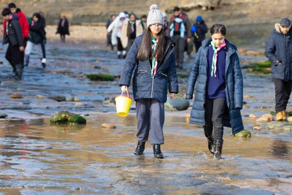 Children walking with buckets on a beach