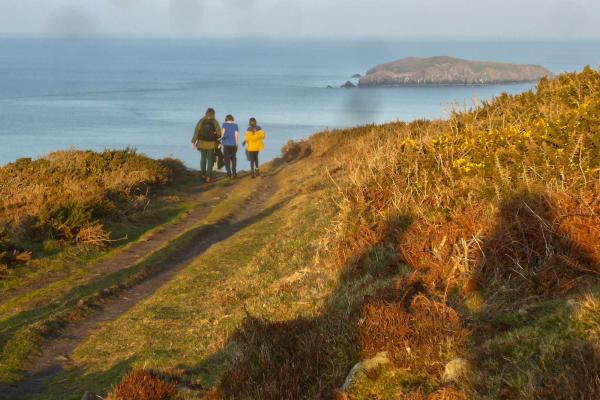 Adult and two children walking along a coastal path
