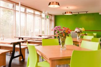 Dining room with green walls, large windows and wooden tables with bench seating and chairs