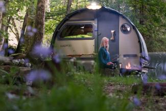 Woman sat by campfire in front of a glamping pod