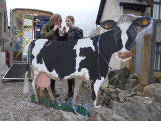 Two people stood next to a cow statue drinking fresh milk