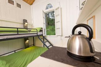 Inside an Anglesey hut at YHA Idwal Cottage Interior of a white painted wooden hut with a bunk bed and kettle on a worktop