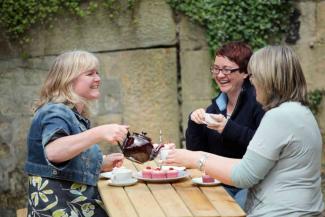 Three women enjoying tea and cake on a bench Three women enjoying tea and cake on a bench