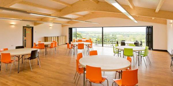 Meeting and function room at YHA Okehampton Bracken Tor with large open windows, round tables and orange chairs