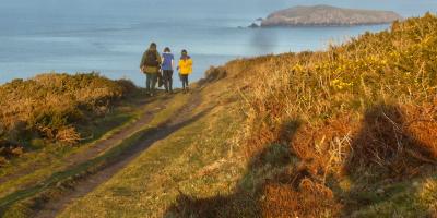 Adult and two children walking along a coastal path