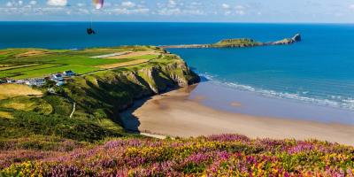 Glider sailing over a beach with blue sea and green cliffs